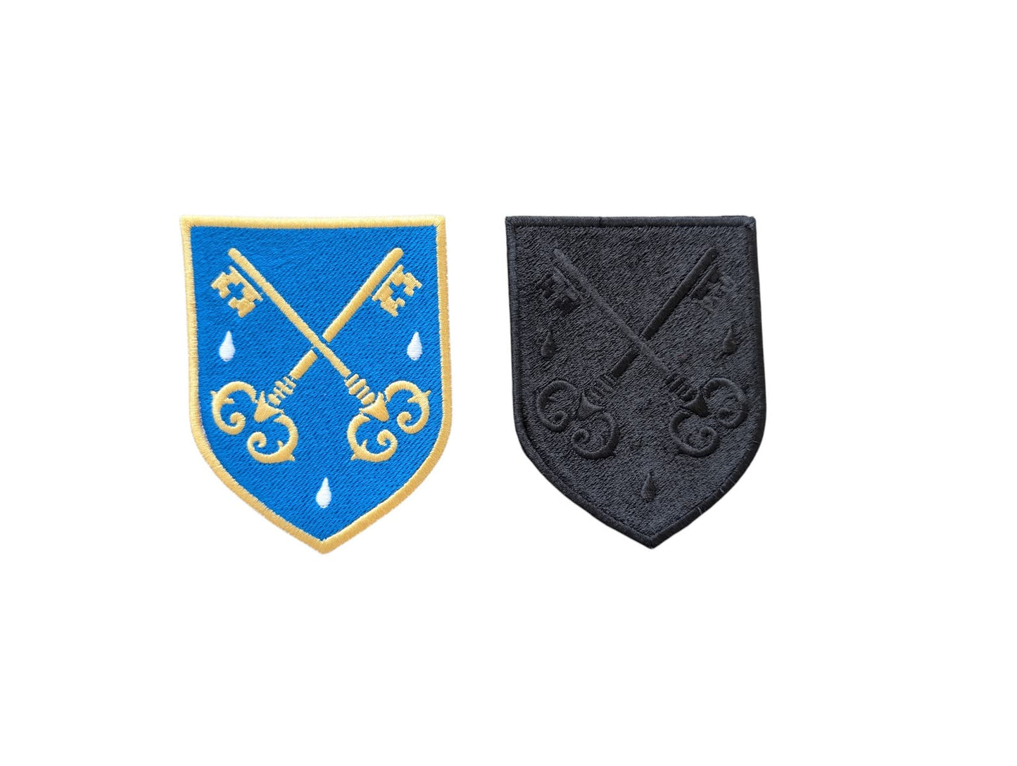 FSSP embroidered badges shown side by side on a white background, with the colour badge featuring a blue background and light-gold crossed keys on the left and the black monochrome badge on the right